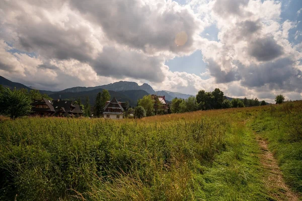 Wide angle view of green grass meadow countryside field with A shaped houses against sleeping knight tatra mountain aka as giewont and dramatic clouds located in Zakopane, South Poland, Europe