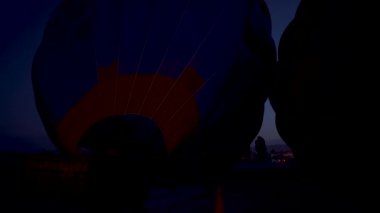 Kapadokya, Türkiye - 14 Eylül 2021: Uçuştan hemen önce bir grup insan tarafından içine ateş püskürtülerek sıcak hava balonunu helyum gazıyla doldurma süreci.