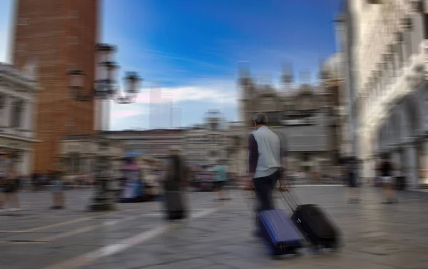 Venice, Italy - September 02, 2018: Panning shot of a tourist man with hat sliding his 2 suitcases in the city center. solo travel concept. motion blurred image.