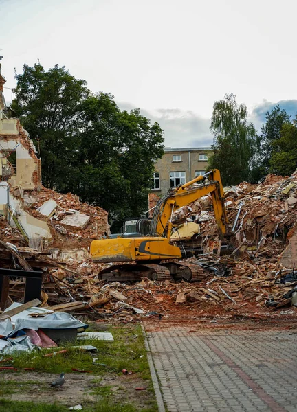 Bulldozer, a type of construction machine with a hydraulically operated shovel on the front and an excavator arm on the back destroying a house apartment building.