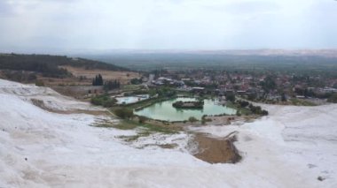 Panning landscape of Pamukkale located in turkey, known for the mineral-rich thermal waters flowing down white travertine terraces on a nearby hillside. close to Hierapolis, an ancient Roman spa city