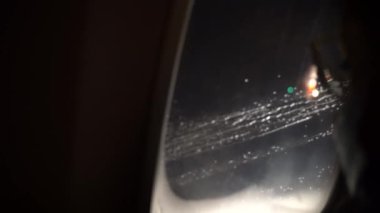 POV of a passenger looking through airplane or flight window during flying in rain at night. Appears to be inflight journey through space, modern air plane speed concept