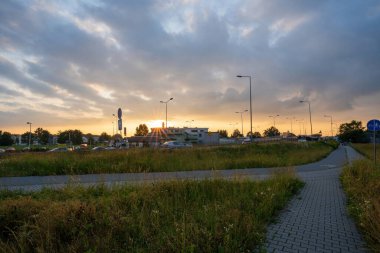 A view of a concrete sidewalk with lanes designated for pedestrian and bicycle traffic joining at a midsection against traffic and dramatic clouds during evening. Traffic coexistance concept.