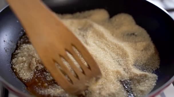 火に熱いフライパンで黒糖を加熱して溶融し 木製のスプーンで混合されます — ストック動画