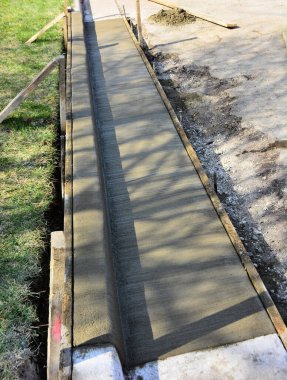 Yapraksız dalların gölgesinin altındaki beton kaldırımlar ve oluklar genişleme ile kesilmiş. Asfalt kaldırma alanındaki pürüzlü kesikler ve çatlaklar eski hasarlı yüzey yerine asfaltı hazırlamak için. Islak çimento.