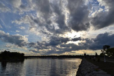 Ludington Park 'ın yansımaları bu Escanaba, Michigan manzaralı katmanlı bulutların iskele sularını fırlatıyor. Güneş çoğunlukla gri ve beyaz bulutlarla birlikte koyu mavi gökyüzünde batıyor. Ağustos görüntüsü alacakaranlıkta kayalık dalgalı dalgalar boyunca çekilir..