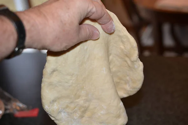 Selective focus on details of the early stages of making pizza dough. The dough is being squeezed between thumb and forefinger to make super thin in the center. Pizza Dough being pinched to make thin in center thinner and larger as the crust forms.