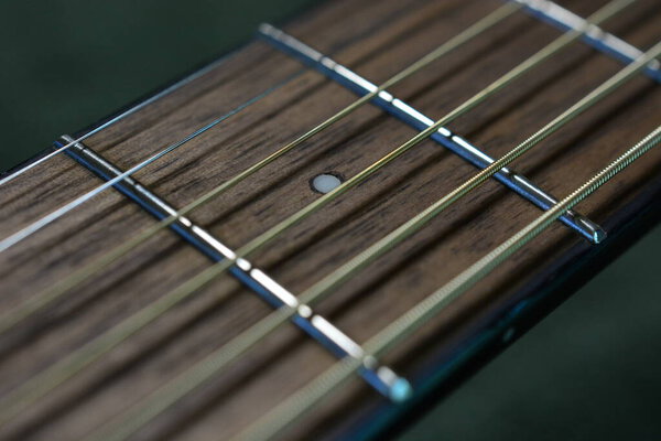 Selective focus on small fifth fret marker dot on a walnut board. Very tight focus includes small sections of the A, D, and G strings.