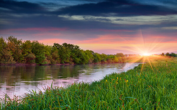 Sunset over flowering meadow by river
