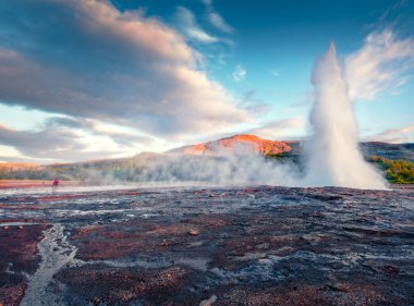 Fotoğrafçı, Laugarfjall Tepesi 'nin yamaçlarındaki Haukadalur vadisinde bulunan Büyük Geysir' in patlamasının fotoğrafını çekiyor. Güneybatı İzlanda, Avrupa 'nın inanılmaz sabah manzarası.