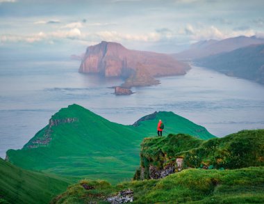 Güzel bir yaz manzarası. Faroe Adaları, Danimarka, Avrupa 'daki Alaberg uçurumlarında gün batımına hayran turistler. Arka planda Vagar Adası olan Mykines Adası 'nın soğuk sabah manzarası. Atlantik Deniz Burnu.