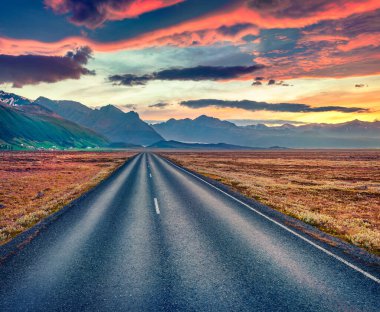 İnanılmaz bir yaz manzarası. Dramatik bulutlu gökyüzü ile boş asfalt yol. İzlanda 'da muhteşem bir gün doğumu. Volkanik tepeleri olan tipik İzlanda manzarası. Seyahat konsepti arka planı