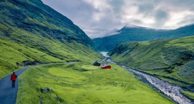 Pollurin Kanyonu 'na giden yolda yürüyen bir turist. Saksun köyünün kasvetli akşam manzarası, Faroe Adaları, Danimarka, Avrupa. Kuzey ülkelerinin acımasız güzelliği. Seyahat konsepti arka planı.