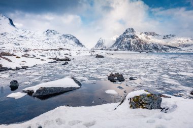 Kutup çevresinde muhteşem bir kış sahnesi. Flakstadoya adasında donmuş fiyort. Lofoten adalarının güzel sabah manzarası Hustinden dağı arka planda, Norveç, Avrupa.