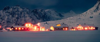 Vestvagoy Adası 'ndaki Utakleiv köyünün panoramik kış manzarası. Geleneksel Norveç evlerinin sıcak akşam aydınlanması. Norveç, Lofoten Adaları 'nın görkemli gece manzarası. Kutup dairesi üzerinde yaşam.