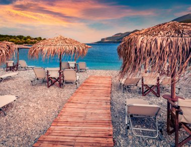 Fokianos sahilinin ahşap iskele ve saman şemsiyeli muhteşem yaz manzarası. Peloponese yarımadasının şaşırtıcı akşam manzarası, Yunanistan, Avrupa. Myrtoan Denizi 'nin muhteşem yaz deniz manzarası.