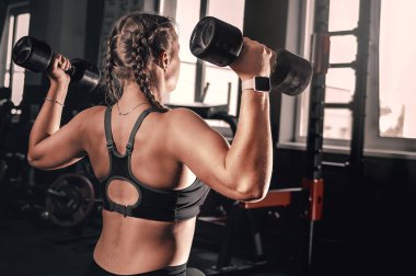 Spor salonunda dambılı genç bir kadın. Spor elbiseli, ağırlıklı halterle spor yapan çekici bir kadının portresi.. 