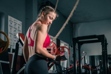 Spor salonunda dambılı genç bir kadın. Spor elbiseli, ağırlıklı halterle spor yapan çekici bir kadının portresi.