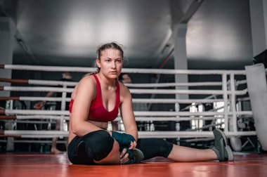Genç ve güzel bir kadın dövüşten sonra ya da boks ringinde egzersiz yaptıktan sonra rahatlıyor. Spor, egzersiz, dövüş sanatları ve rahatlama konsepti. Boks ringinde oturan kadın dövüşçü.