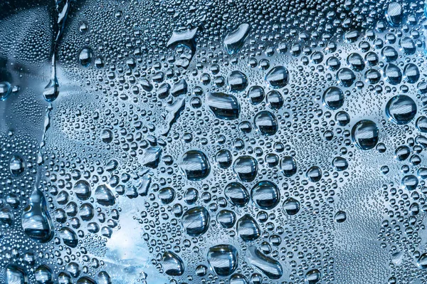 Su damlaları mavi arkaplanda. Cam yüzeydeki su damlacıkları.