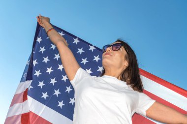 Elinde Amerikan bayrağı sallayan gülümseyen genç bir kadının portresi. ABD 4 Temmuz 'u kutluyor. Vatansever genç kadın güzel bir tarlada Amerikan bayrağı dalgalandırıyor.. 