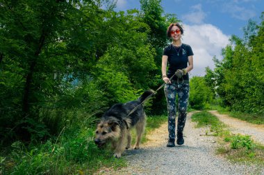 Köpeğini tasmayla gezdiren neşeli genç bir kadın. Kız köpekle gezerken eğleniyor. Arkadaşlık, rahatlık, evcil hayvan konsepti.. 