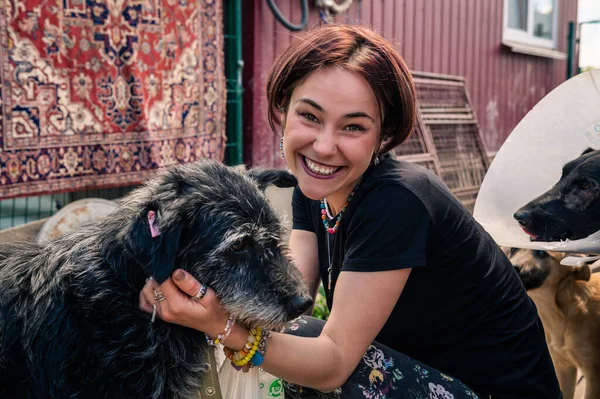 Dog at the shelter. Animal shelter volunteer takes care of dogs. Lonely dogs in cage with cheerful woman volunteer.