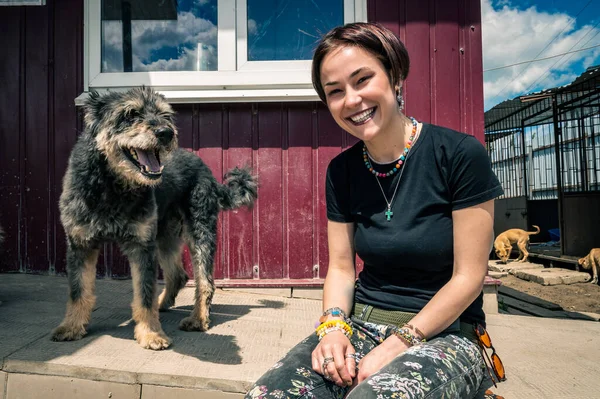 Animal shelter volunteer takes care of dogs. Lonely dogs in cage with cheerful woman volunteer. Dog at the shelter.