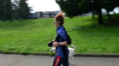 RIVNE, UKRAINE - 29 Eylül 2022. Fit dişi, komik köpeğiyle koşar. Şehir parkında köpeklerle yarışmak. Şehir parkında koşmak. 