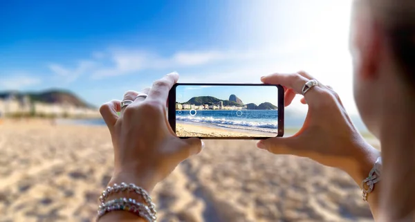 Woman in Copacabana Beach taking a photo with her mobile phone. Photographing with a camera of a smartphone in Rio de Janeiro, Brazil.