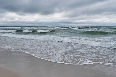 Gelen dalgalarla güzel deniz manzarası, dramatik bulutlu gökyüzü, kumlu sahil.