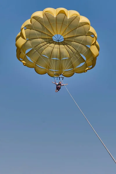 Femme blanche âgée est parasailing.She vole sous parachute jaune dans le ciel bleu, souriant et ouvrant les bras. — Photo