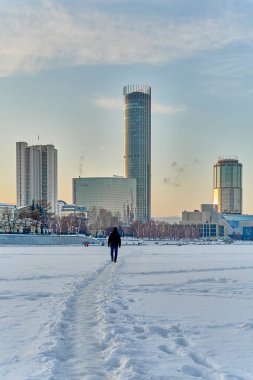 Yekaterinburg, Rusya-22 Ocak 2022 Kış Şehri 'nde gün batımı. Karla kaplı gölette yürüyen bir adam. Kuleler Iset, Demidov, Otel, Bölgesel Duma, Drama Tiyatrosu' nun simgeleri.