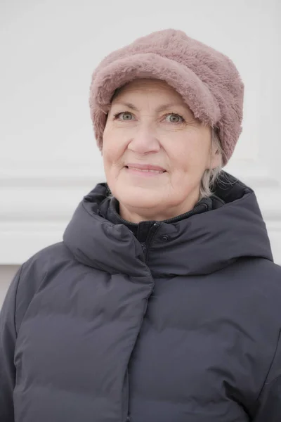 カメラを見て笑顔のシニア女性のクローズアップ冬の肖像画は フェイクピンクの毛皮の帽子と青いダウンジャケットを着て 高齢者概念 — ストック写真