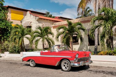 Varadero, Küba - 10 Şubat 2022: 1957 model kırmızı beyaz Chevrolet arabalı adam tatil köyünün caddesinde oturuyor.
