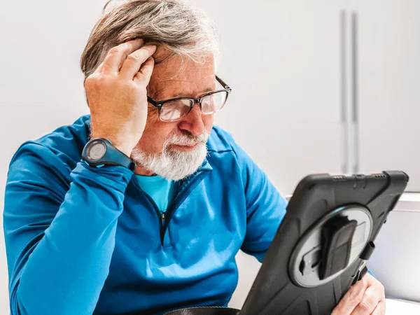 senior seated man looks worriedly at the tablet