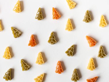 Beyaz arka planda çiğ buğday makarnasından yapılmış Noel ağaçları deseni. Düz yerde, üst tarafta. Kış sanatı gıda konsepti.