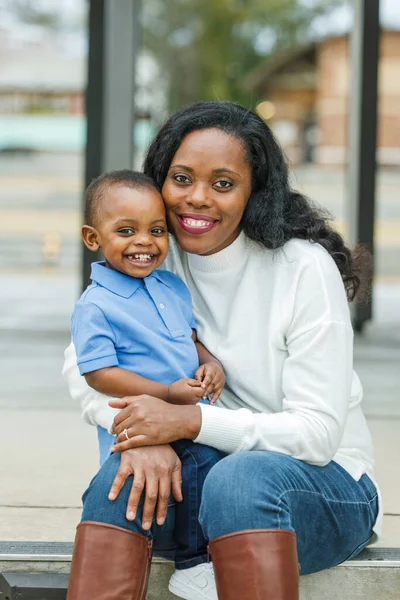 Красивая афро-американская мама сидит на ступеньках и обнимает своего сына-малыша, и они оба улыбаются и счастливы. — стоковое фото