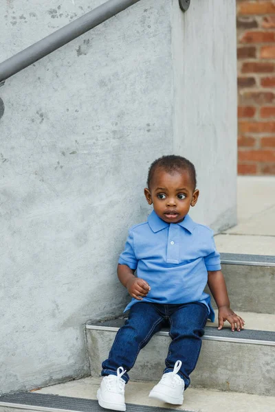 Милый годовалый младенец почти дошкольного возраста афроамериканец с большими глазами, сидящий на ступеньках города — стоковое фото