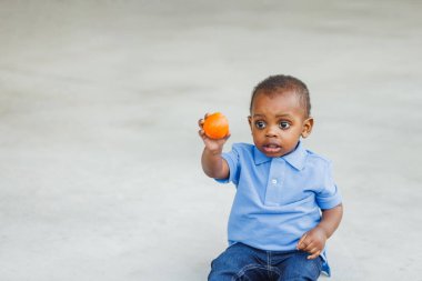 Sevimli bir çocuk, anaokulu çağında, Afro-Amerikan bir çocuk elinde sağlıklı bir portakal tutuyor.