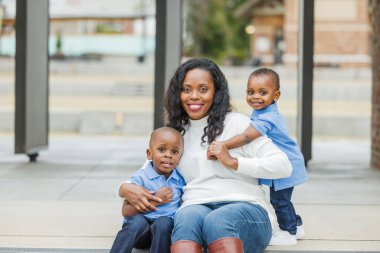 Dışarıda iki oğluyla oturan uzun saçlı bir anne.