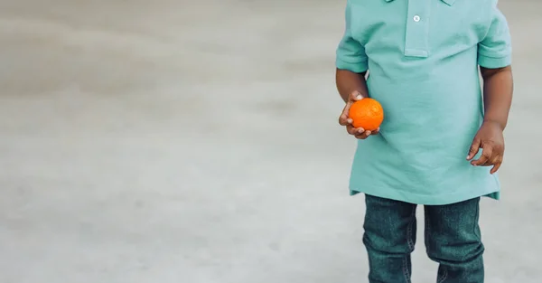 Милый годовалый малыш почти дошкольного возраста афроамериканец держит здоровую закуску апельсина — стоковое фото