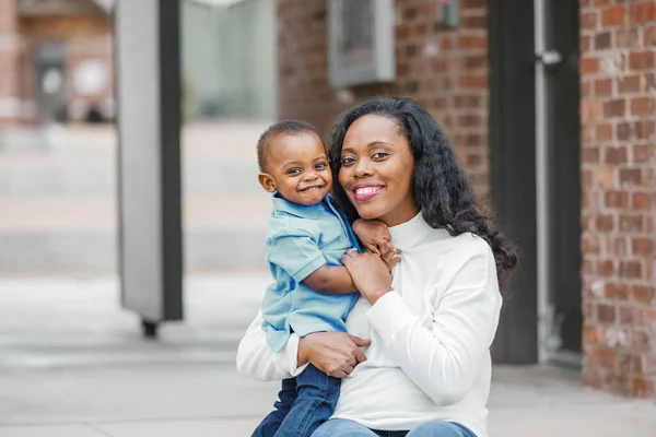 Красивая афро-американская мама сидит на ступеньках и обнимает своего сына-малыша, и они оба улыбаются и счастливы. — стоковое фото