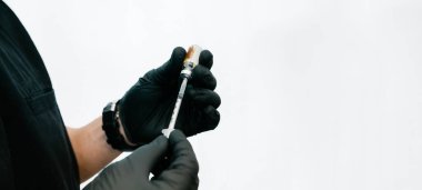 Siyah önlük ve eldiven giyen bir tıbbi hizmet sağlayıcının beyaz bir zemin ile doldurduğu şırıngayı fotokopi aletiyle kapatın.