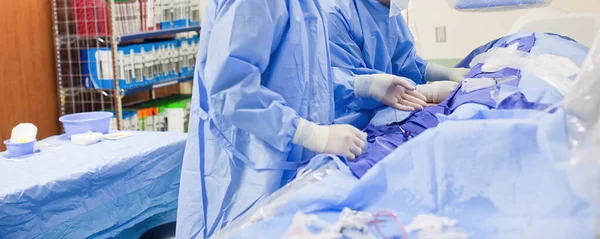 Dos médicos cirujanos no descritos que realizan una cirugía en una sala quirúrgica con uniformes quirúrgicos azules y guantes de látex blanco —  Fotos de Stock