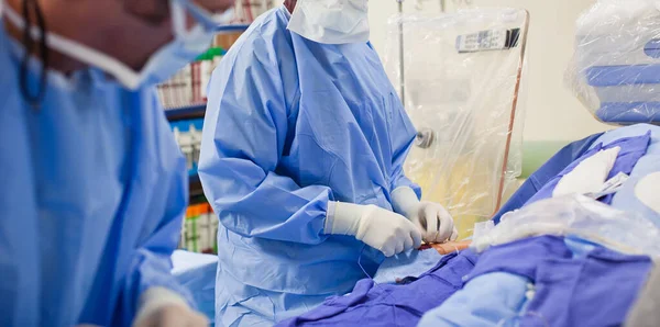 Two non-descript surgeon doctors doing a surgery in a surgical room wearing operating blue scrubs and white latex gloves