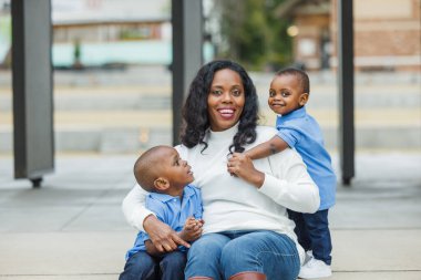 Dışarıda iki oğluyla oturan uzun saçlı bir anne.