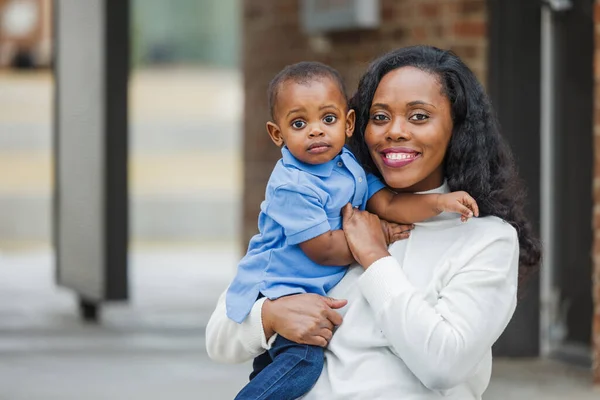 Красивая афро-американская мама сидит на ступеньках и держит своего маленького мальчика, и он выглядит грустным. — стоковое фото