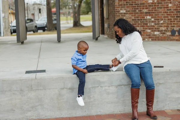 Мама помогает сыну завязывать шнурки на улице. — стоковое фото