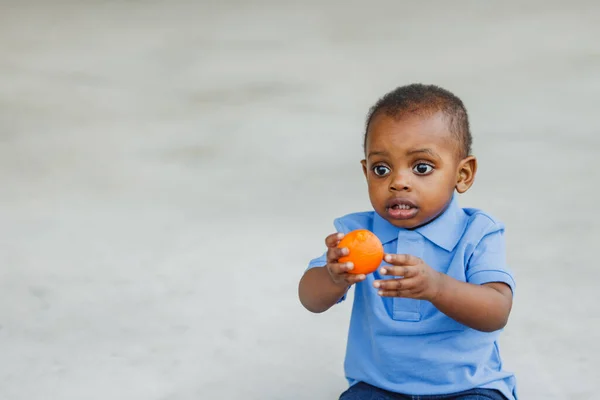 Милый годовалый малыш почти дошкольного возраста афроамериканец держит здоровую закуску апельсина — стоковое фото